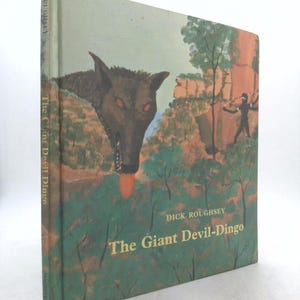 May include: A vintage hardcover book titled "The Giant Devil-Dingo" by Dick Roughsey. The cover features a painted illustration of a dingo with red eyes and a long tongue, set against a landscape with a figure.