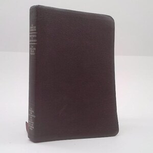 May include: A dark brown book with text on the spine. The book has a smooth, leather-like cover and appears to be a hardcover edition. The spine features printed text in a vertical orientation, with a red bookmark.