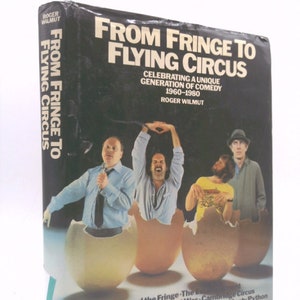 May include: A book cover with a black background and the title "From Fringe to Flying Circus: Celebrating a Unique Generation of Comedy 1960-1980" by Roger Wilmut. The cover features a photo of four men in eggshells, with the text "Beyond the Fringe - The  - Cambridge Circus - That Was The Week That Was - The Goodies - Monty Python - I'm Sorry I'll Read That Again" at the bottom.
