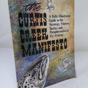 May include: A book titled The Curtis Creek Manifesto, A Fully Illustrated Guide to the Strategy, Finesse, Tactics and Paraphernalia of Fly Fishing by Sheridan Anderson. The cover features a large fish, a fly, and a cartoon angler on a textured background.