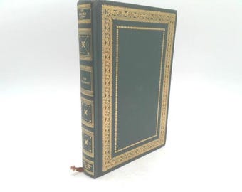 May include: A hardcover book with a dark green cover and gold decorative accents. The spine features the title "THE TALISMAN" and author "SIR WALTER SCOTT" in gold lettering. A brown bookmark is visible.