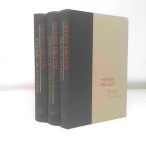 May include: A stack of four books by Henry Miller. The spines are black with orange text. The book titles include "Tropic of Cancer", "Tropic of Capricorn", "10 A.M. & After", and "Black Spring". The cover of "Black Spring" is beige.