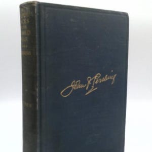 May include: A dark blue hardcover book with a gold embossed signature of John J. Pershing on the front cover. The spine features gold text that reads My Experiences in the World War by John J. Pershing, Volume II, with a worn and aged appearance.
