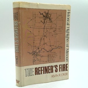 May include: A hardcover book titled The Refiner's Fire by Alvin R. Dyer. The dust jacket features a tan background with a black line-drawn map of Missouri, a legend, and the title printed in bold brown text on the front and the spine.