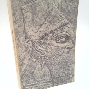 May include: A vintage book titled "The Essence Book of Asia" with a gray and white cover. The cover features a detailed relief of a bearded face wearing a headdress. The book's spine is off-white.