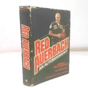 May include: A hardcover book titled "Red Auerbach: An Autobiography." The cover features a photo of Red Auerbach holding a basketball, with the text in red and white. The book is a biography.