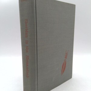 May include: A hardcover book titled "Sheridan in the Shenandoah" with a gray cover and red text. The spine displays the title and author's name, while the front cover features a red illustration.