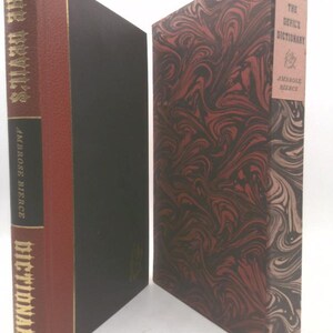 May include: Two hardback books with marbled covers. The book on the left is titled "The Devil's Dictionary" by Ambrose Bierce. The book on the right has a black and red marbled cover with the title "The Devil's Dictionary" and the author's name, "Ambrose Bierce".