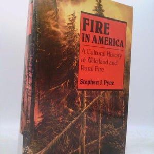 May include: A hardcover book titled "Fire in America" with a red title box. The cover features a forest scene with tall trees and a fiery, smoky sky. The book is a cultural history of wildland and rural fire by Stephen J. Pyne.