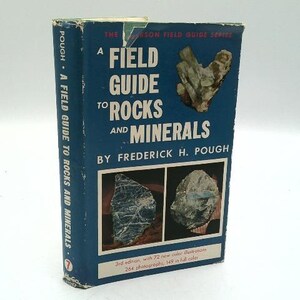 May include: A Field Guide to Rocks and Minerals by Frederick H. Pough. The book has a blue cover with white text and images of rocks. The spine reads "A Field Guide to Rocks and Minerals" vertically. The book is a 3rd edition.