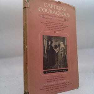 May include: A vintage book titled "Captions Courageous" with a pink cover and text in white. The book features an image of two people in historical attire and text that reads "Tell the press we're just good friends."