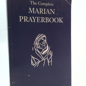 May include: A navy blue book titled "The Complete Marian Prayerbook" with white lettering. The cover features a line drawing of a woman and child. The book's spine is visible on the left side.