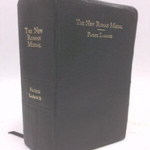 May include: A black hardcover book titled "The New Roman Missal" with gold lettering. The author's name, "Father Lasance," is also in gold. The book has a textured cover and a black ribbon bookmark.