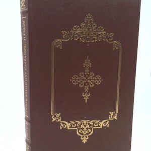 May include: A burgundy leather-bound book with gold lettering on the spine that reads "Ectopic Pregnancy and Other Works". The front cover features a gold ornate design.