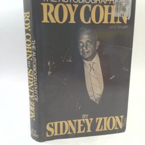 May include: A hardcover book titled "THE AUTOBIOGRAPHY OF ROY COHN" by Sidney Zion. The cover is black with gold lettering and a portrait of a man in a suit. The book's spine also features the title and author's name.