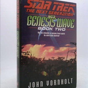 May include: A paperback book cover with a dark blue background and a red and green title: "Star Trek: The Next Generation - The Genesis Wave, Book Two". The cover features a dark forest scene with glowing yellow eyes in the foreground. The author's name, "John Vornholt", is printed in white at the bottom of the cover.