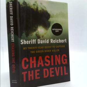May include: A black hardcover book with a red title, "Chasing the Devil", and a photo of a foggy lake on the cover. The book is by Sheriff David Reichert and is about his twenty-year quest to capture the Green River Killer. The book is an autographed copy.