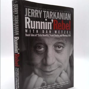 May include: A hardcover book titled "Jerry Tarkanian Runnin' Rebel" with a black and white image of a man on the cover. The book's title is in large white and red letters. The book's spine reads "Jerry Tarkanian Runnin' Rebel".