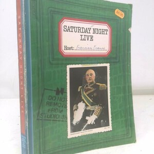 May include: A vintage book titled "Saturday Night Live" with a green cover and a photo of Francisco Franco. The cover features the show's title and host's name in a red and white label. The book has a price sticker.