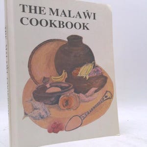 May include: A hardcover cookbook titled "The Malawi Cookbook" with a cream-colored cover. The cover features an illustration of various food items and cooking utensils in shades of brown, orange, and pink. The title is in bold, black letters.