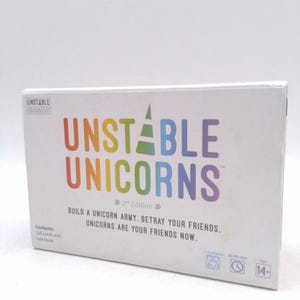 May include: A white box with the text "Unstable Unicorns" in rainbow colors. The box is for a card game with a unicorn theme. The text on the box says "Build a unicorn army. Betray your friends. Unicorns are your friends now."