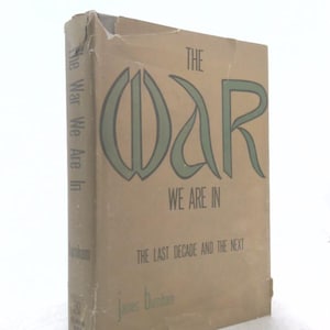 May include: A hardcover book titled The War We Are In: The Last Decade and the Next by James Burnham. The dust jacket is tan with dark green lettering and a stylized graphic design. The edges of the dust jacket show signs of wear and tearing.