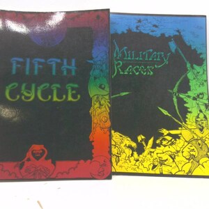 May include: Two game books with colorful covers. The left book has a black cover with the text "FIFTH CYCLE" in rainbow colors. The right book has a blue cover with the text "Military Racers" in green.