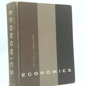 May include: A hardcover book titled "Economics" by Paul A. Samuelson. The book's cover features vertical stripes in shades of brown, gray, and black. The title is in white, and the spine displays the title and publisher.