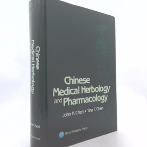 May include: A black hardcover book titled Chinese Medical Herbology and Pharmacology by John K. Chen and Tina T. Chen. The front cover features the title in white text, a small blue logo, and the publisher name Art of Medicine Press.