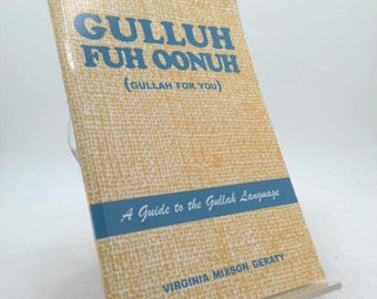 May include: A book titled "GULLUH FUH OONUH (GULLAH FOR YOU)" is displayed on a clear stand. The cover has a textured, light yellow background with blue text. A blue band across the middle reads "A Guide to the Gullah Language". The author's name is "VIRGINIA MIXSON GERATY".