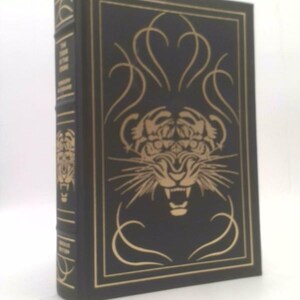 May include: A black leather-bound book with gold lettering and a gold tiger illustration on the front cover. The title of the book is "The Tiger Rising".