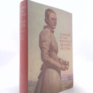 May include: A hardcover book titled A History of the Writings of Beatrix Potter with a red spine and a front cover featuring a portrait of a person in a high-collared dress holding flowers against a landscape background with printed text.