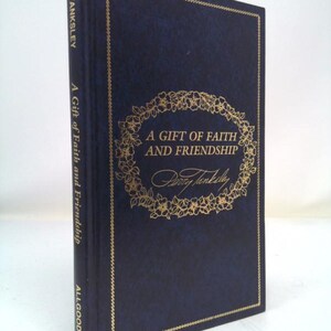 May include: A hardcover book with a dark blue cover and gold accents. The title "A Gift of Faith and Friendship" is displayed in gold script within a floral wreath. The author's name, Perry Tanksley, is also in gold.