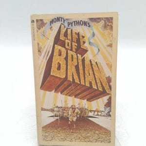 May include: A paperback book titled "Monty Python's Life of Brian." The cover features large, 3D block letters spelling out the title, with a figure running towards a crowd. The background is a warm, golden color with radiating light.