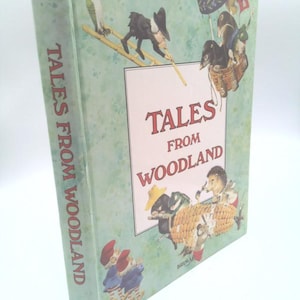 May include: A hardcover book titled "Tales From Woodland" with illustrations of woodland creatures. The cover is light green with a white rectangle containing the title in red. The spine reads "Tales From Woodland".
