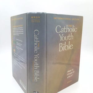 May include: A hardcover book titled "The Catholic Youth Bible" in a gray cover. The book is an international edition and features the text "Pray It, Study It, Live It." The spine reads "NRSV Catholic Edition."