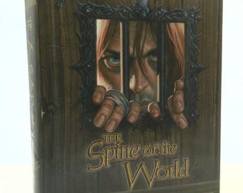 May include: A book cover with a dark brown wooden background. The title "The Spine of the World" is written in gold lettering. The author's name, "R.A. Salvatore", is also written in gold lettering. The cover features a man with long brown hair looking through a barred window. The text "Forgotten Realms" is in a gold banner at the top of the cover.