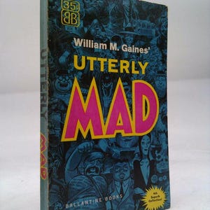 May include: A vintage paperback book titled "Utterly Mad" by William M. Gaines. The cover features a blue background with cartoon illustrations and the word "MAD" in large pink letters. Published by Ballantine Books.