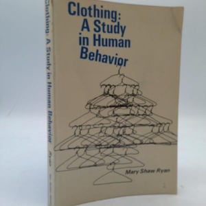 May include: A vintage book titled "Clothing: A Study in Human Behavior" with blue text on a beige cover. The cover features a drawing of stacked coat hangers. The author's name, Mary Shaw Ryan, is also visible.