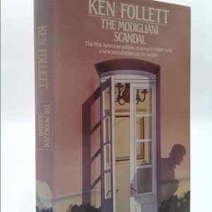 May include: A book cover with a pink and white background. The title is "The Modigliani Scandal" by Ken Follett. The cover features a painting of a door with a window and a shadow of a person.