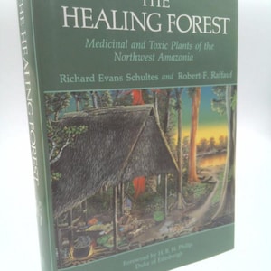 May include: A hardcover book titled The Healing Forest: Medicinal and Toxic Plants of the Northwest Amazonia by Richard Evans Schultes and Robert F. Raffauf. The dark green cover features an illustration of a thatched hut in a forest.