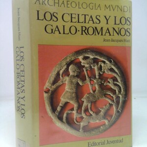 May include: A hardcover book titled "LOS CELTAS Y LOS GALO-ROMANOS" by Jean-Jacques Hatt. The cover features a bronze-colored circular relief with figures and text in Spanish. The book has a light green spine and a red background.