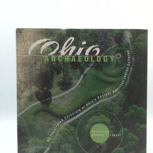 May include: A book titled Ohio Archaeology: An Illustrated Chronicle of Ohio's Ancient American Indian Cultures by Bradley T. Lepper. The cover features an aerial view of a green landscape with a winding path and a map overlay on the left side.
