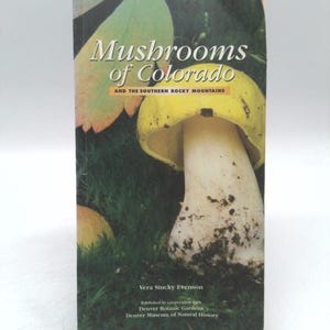 May include: A book titled "Mushrooms of Colorado" with a photograph of a yellow and white mushroom on the cover. The book's title is in a stylized font, and the author's name and publisher are listed below.