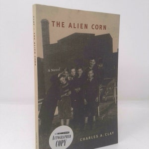 May include: A book cover with a black and white photo of a group of boys standing in front of a building. The book title is "The Alien Corn" by Charles A. Clay. The book is an autographed copy.