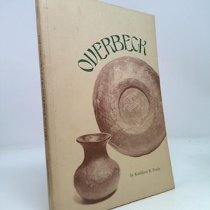 May include: A book titled "Overbeck" with a beige cover. The cover features a large illustration of a pottery piece and a smaller vase. The title is in green, and the author's name is visible.