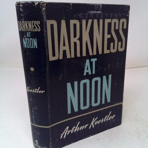 May include: A vintage hardcover book titled "Darkness at Noon" by Arthur Koestler. The book has a dark blue cover with the title in large, light-colored letters and the author's name in white script. The book is slightly worn.