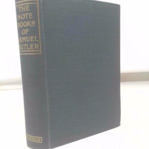 May include: A hardcover book titled "The Note Books of Samuel Butler." The book has a dark green cover with gold lettering on the spine. The book is standing upright on a white surface.