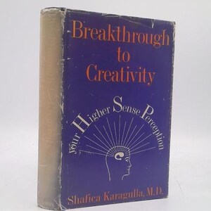 May include: A hardcover book titled "Breakthrough to Creativity" with a blue cover and orange lettering. The book features the phrase "Your Higher Sense Perception" and the author's name, Shafica Karagulla, M.D.