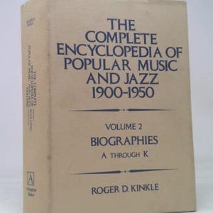 May include: A vintage book titled "The Complete Encyclopedia of Popular Music and Jazz 1900-1950." Volume 2, subtitled "Biographies A through K," is displayed. The book has a beige cover with dark blue text.